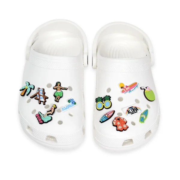 White Crocs decorated with Hawaiian-themed shoe charms, including hula dancers, pineapples, surfboards, and tropical designs.