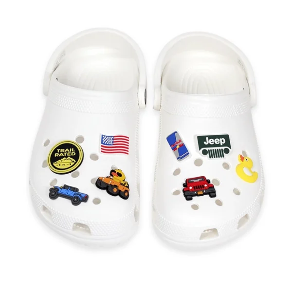 White Crocs decorated with Jeep-themed shoe charms, including a Jeep grille, trail-rated badge, red and blue Jeep icons, an American flag, a rubber duck, and a Red Bull can.